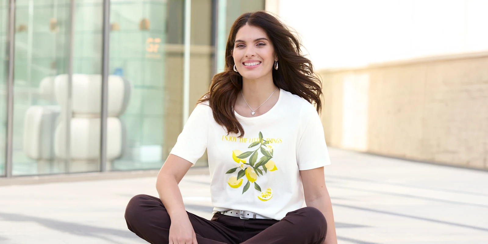 Ein Model mit langen dunklen Haaren trägt ein weisses T-Shirt mit Zitronenmotiv und eine Hose.