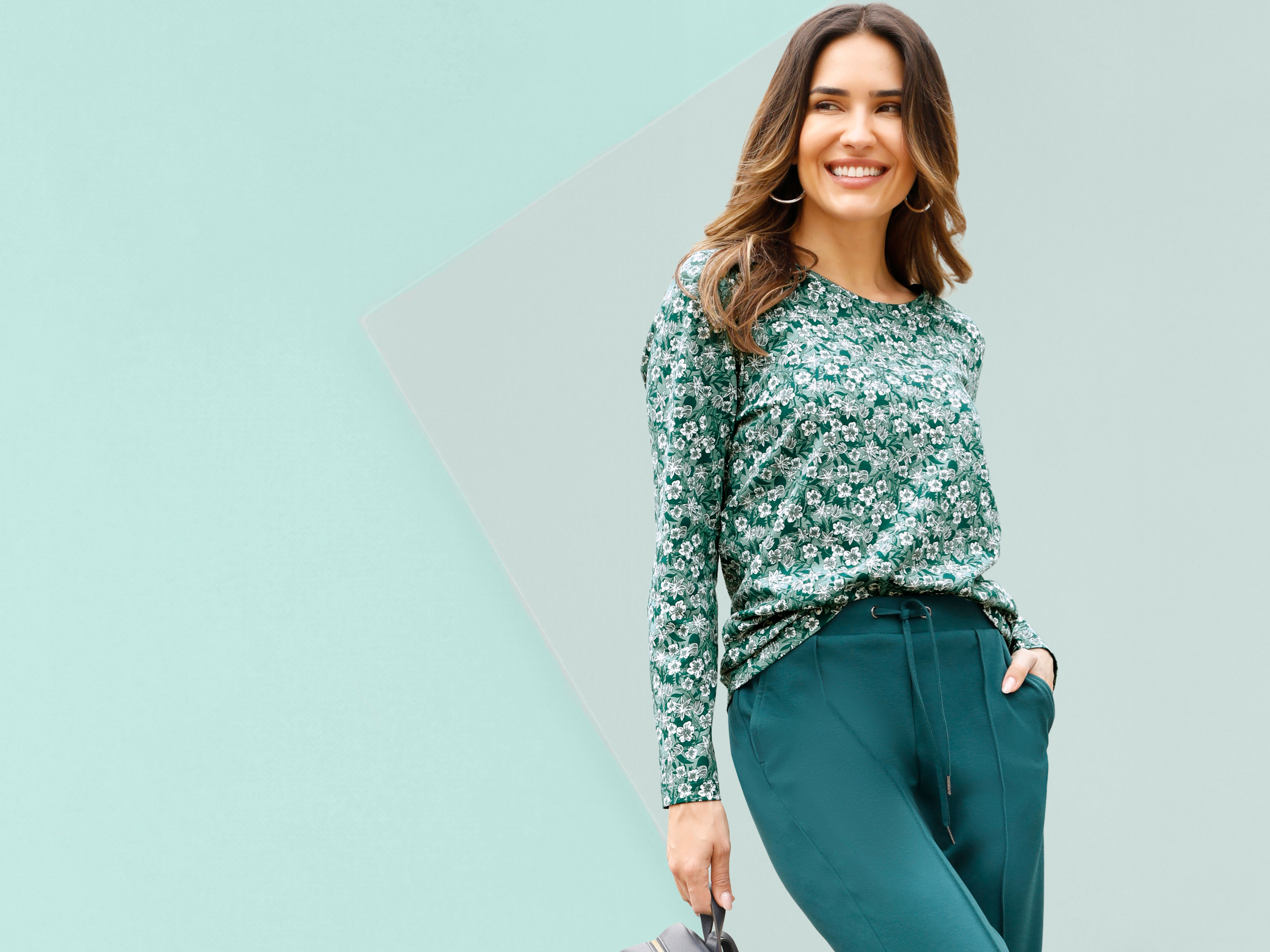 Model má na sebe zelené tričko s dlhým rukávom s bielym kvetinovým vzorom a tmavozelené nohavice so sťahovacou šnúrkou.