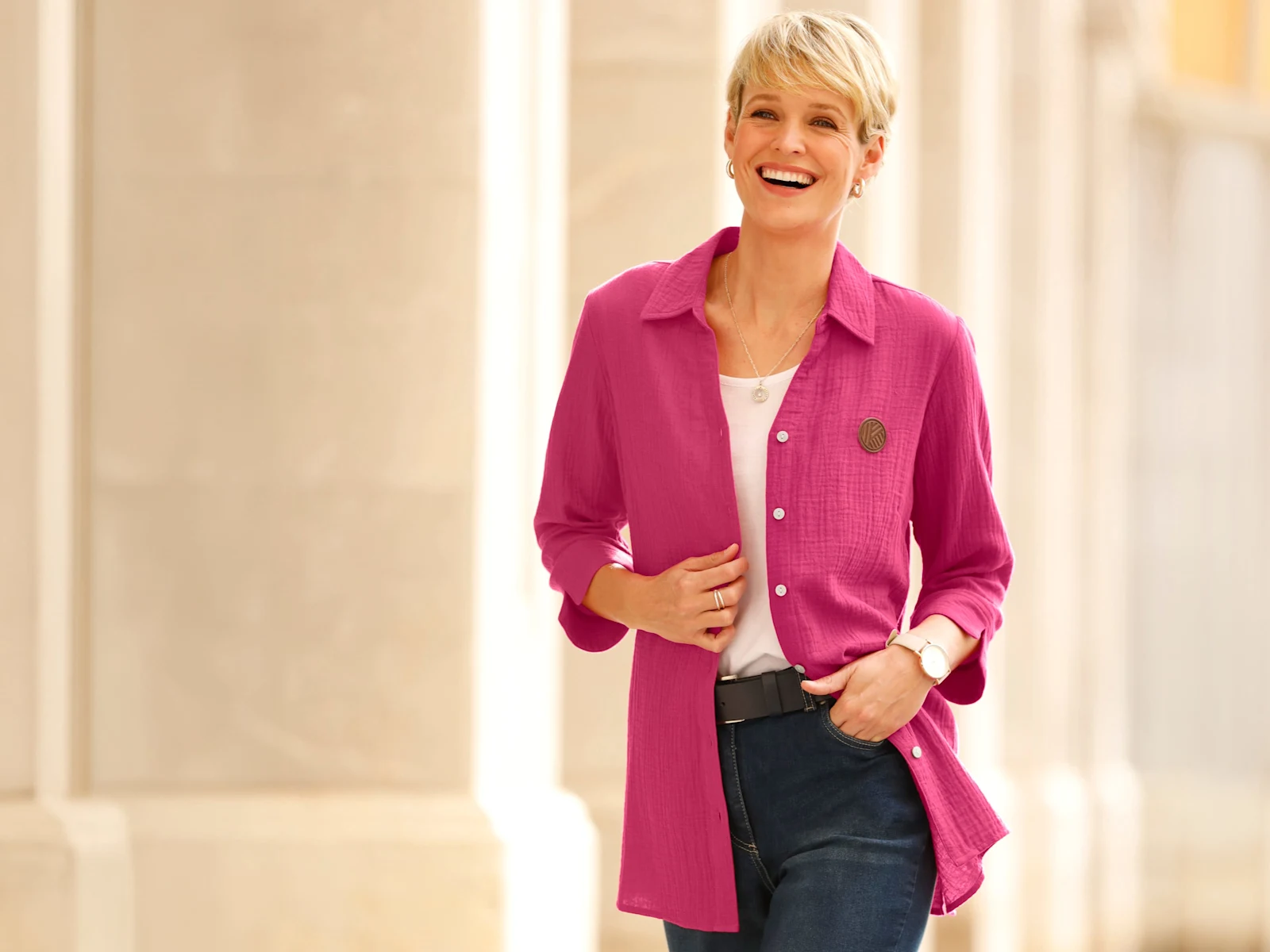 Model má na sobě růžovou dlouhou košili přes bílé tričko a modré džíny.