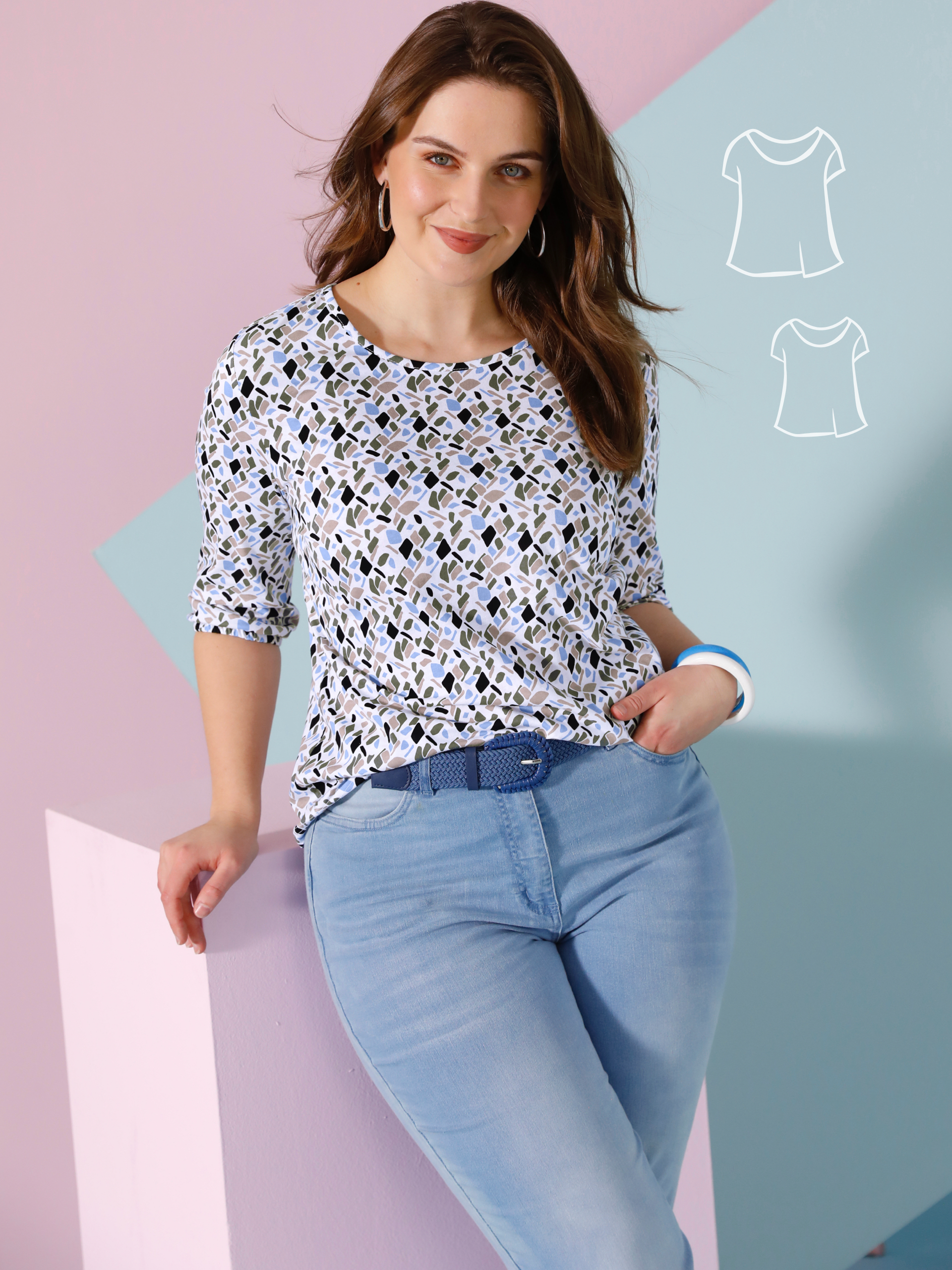 Ein Model lehnt an einem pastellfarbenen Würfel, trägt ein gemustertes, weißes Oberteil und hellblaue Jeans mit blauem Gürtel.