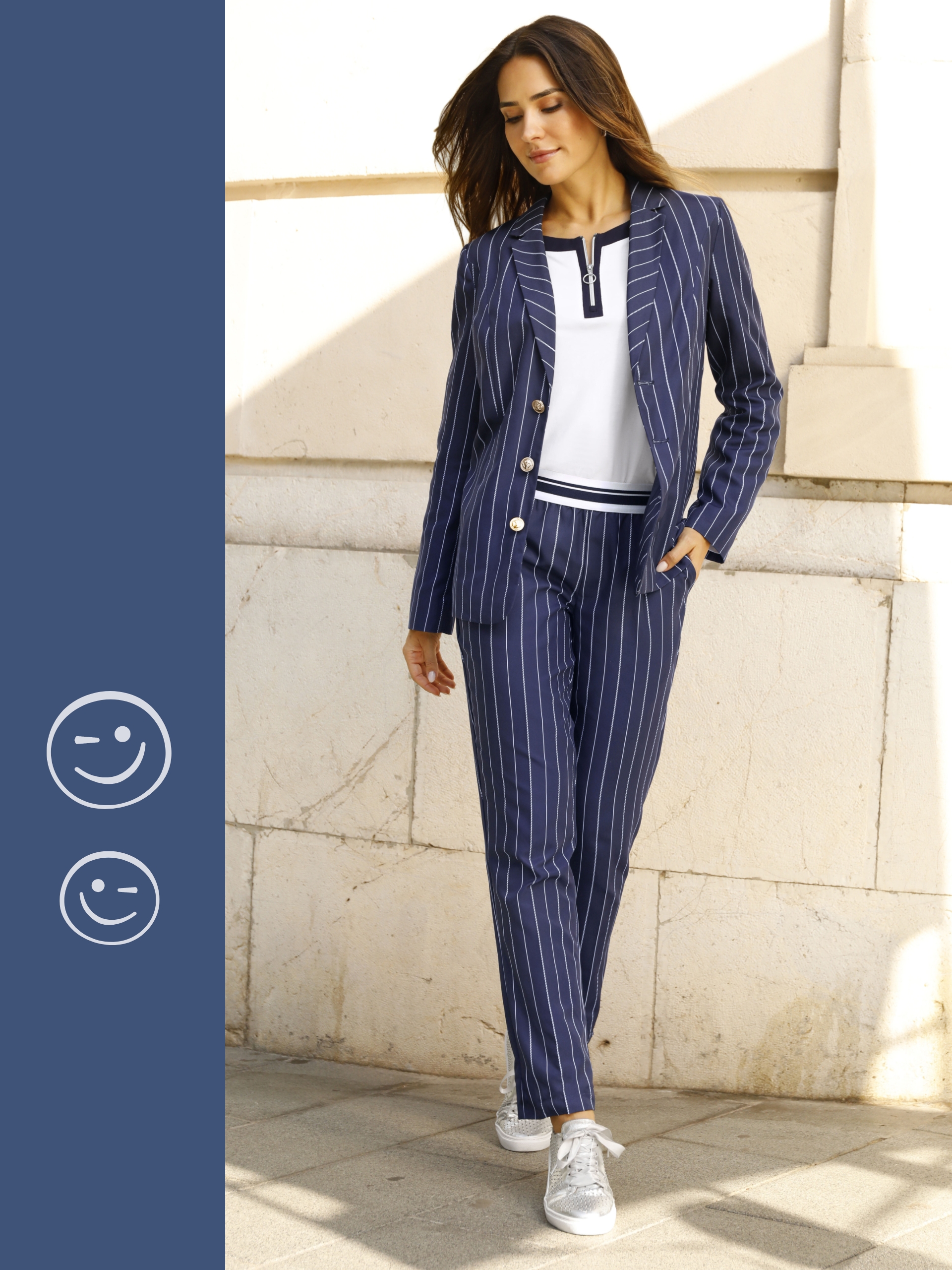 Een model draagt een donkerblauw pak met witte krijtstrepen, gecombineerd met een wit shirt en witte sneakers.
