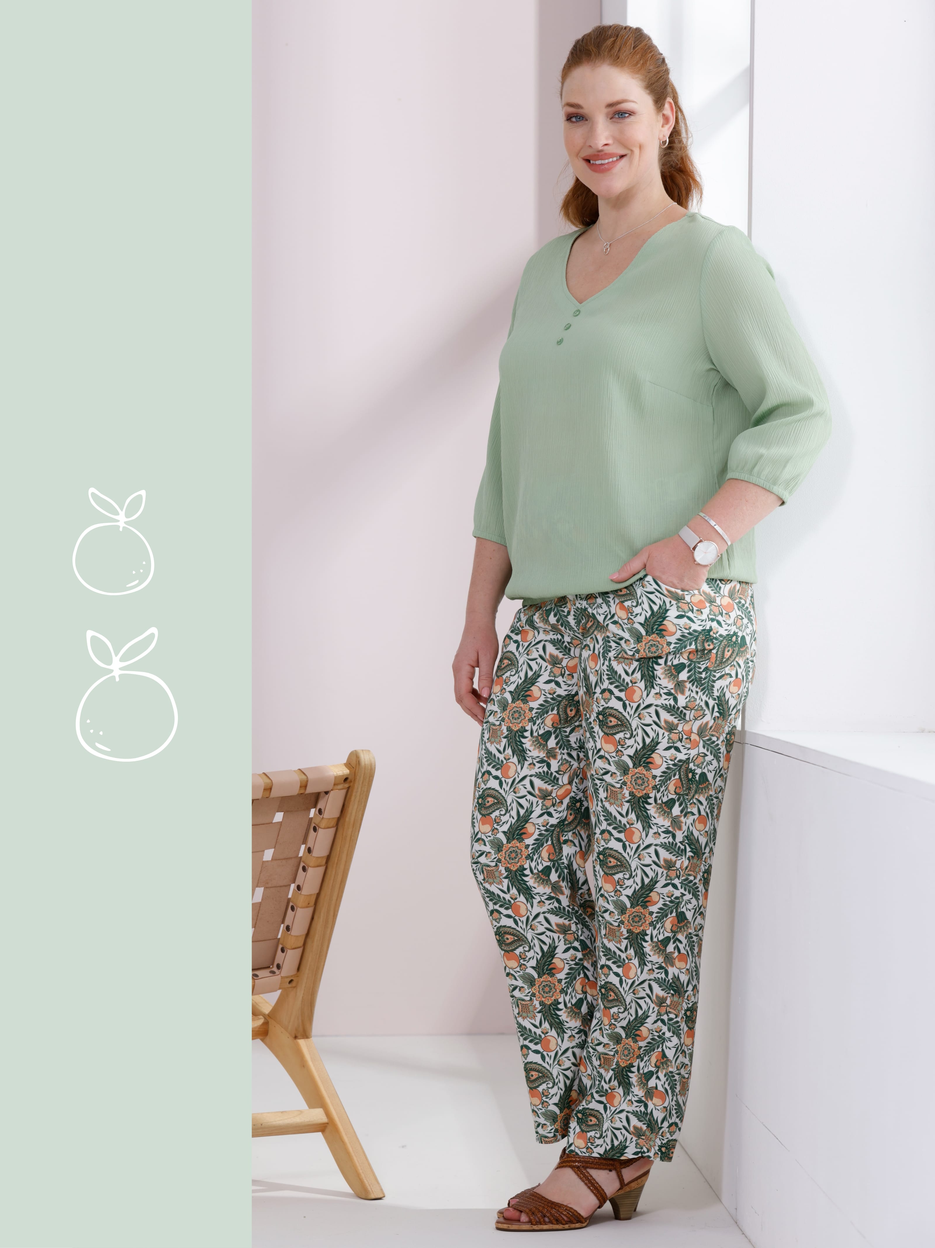 Ein Model trägt einen mintgrünen Pullover und gemusterte, weite Hose.