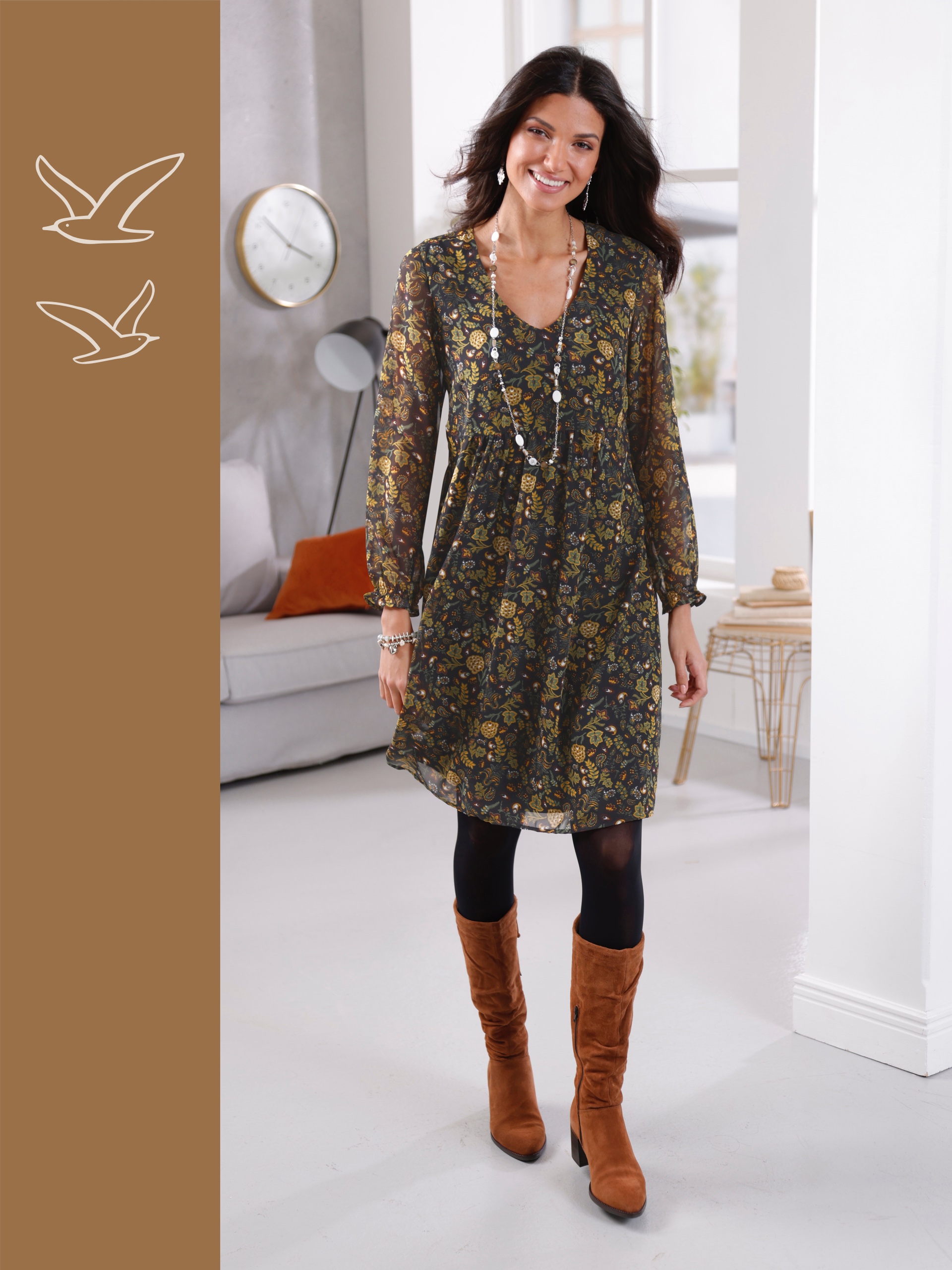 Ein Model trägt ein florales Kleid mit langen Ärmeln und braunen Stiefeln. Sie hat eine lange Kette um den Hals. Der Hintergrund ist modern und hell.