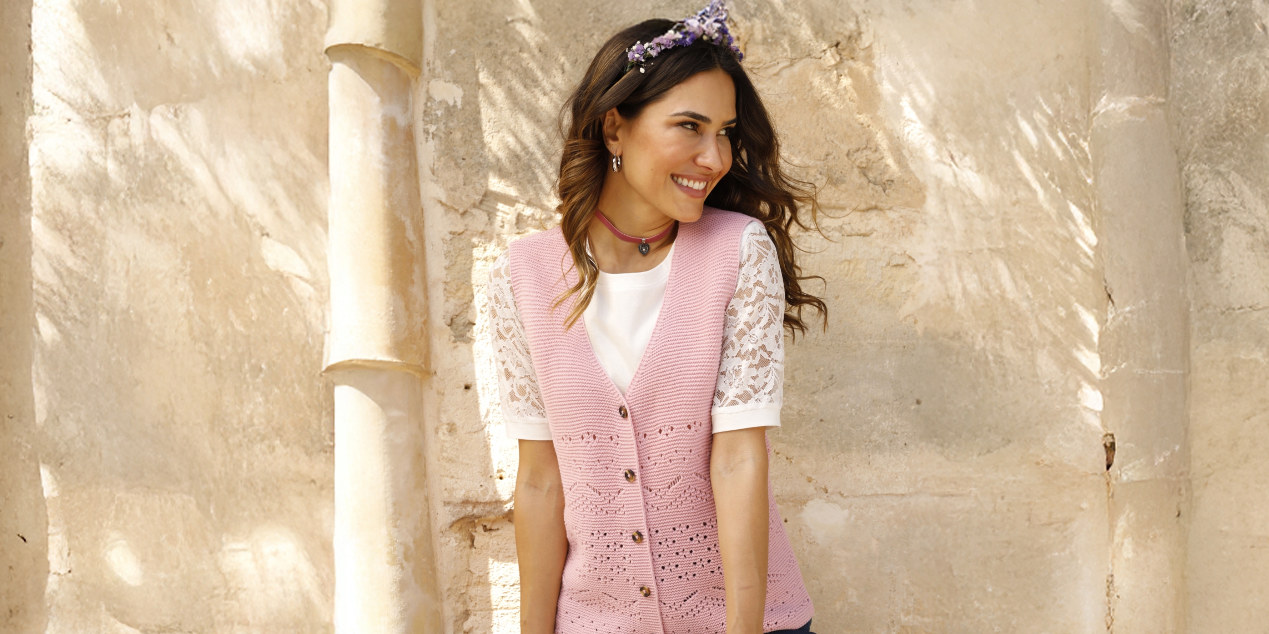Modelka má na sebe bielu blúzku a ružovú pletenú vestu pred svetlým pozadím.