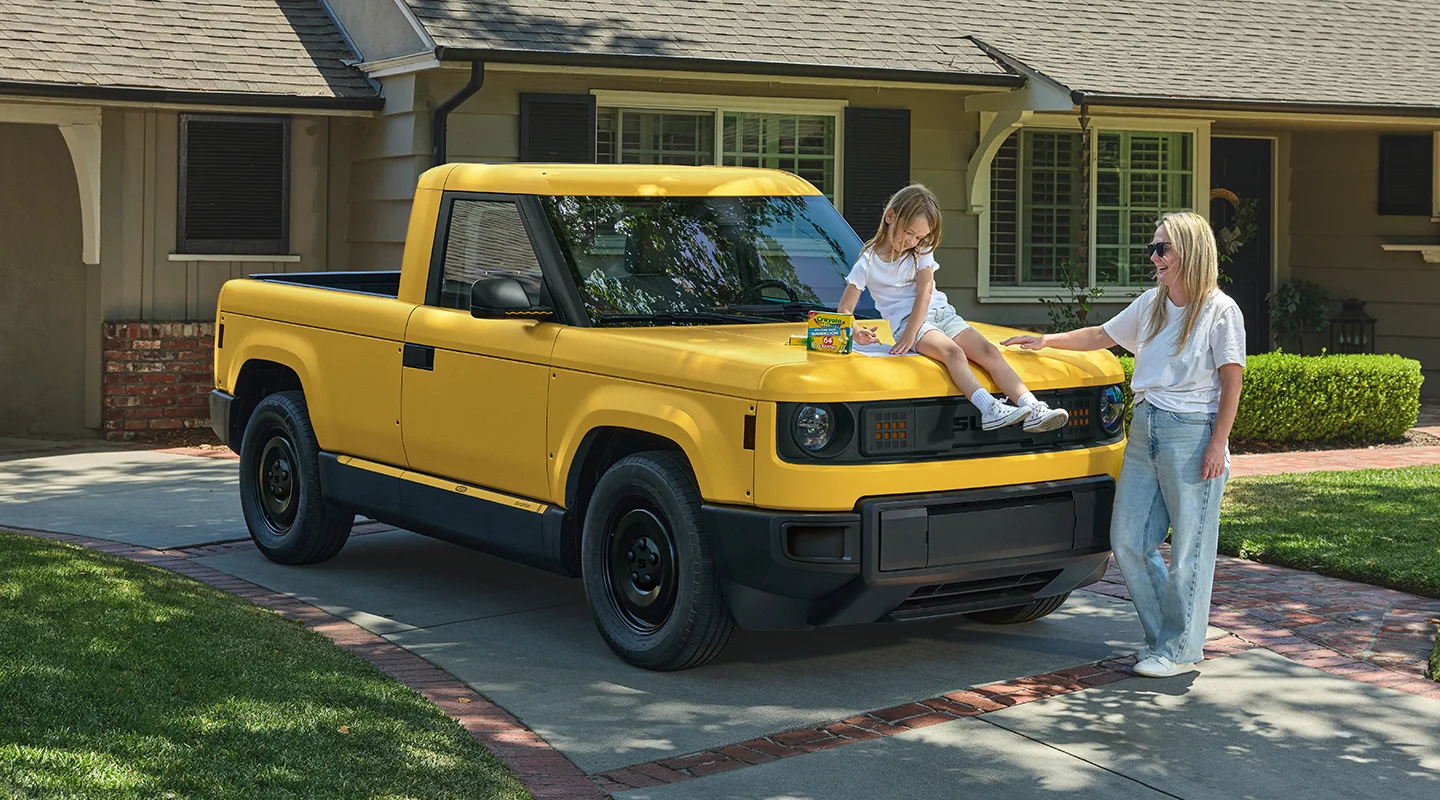 Girl sitting on hood of yellow Slate truck in driveway