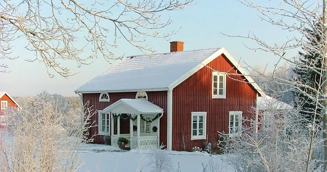 Et af de mange feriehuse der udlejes via NOVASOL. Her ses den røde hytte en smuk vinterdag iklædt sne.