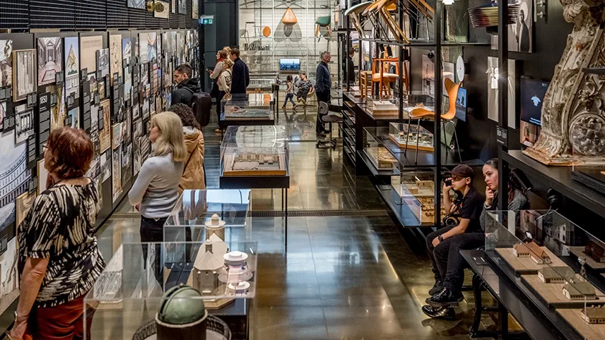 Bild från en av utställningarna. Man ser hyllor och montrar med bland annat prydnadsföremål och möbler, och besökare strosar omkring, står och tittar eller sitter ner på bänkar.