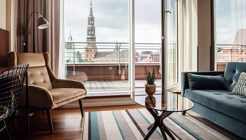 Bild från en av hotellets juniorsviter med en smakfull sittgrupp mot ett stort fönster och en öppen balkongdörr. Utanför fönstret syns Michaelskyrkan.