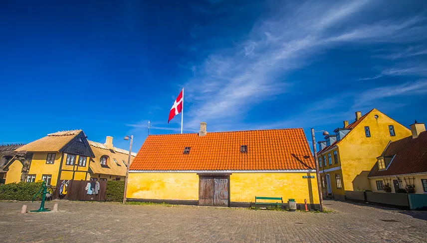 Bild från Dragörs stadskärna med ett gammalt stenhus med gul puts och en hissad dansk flagga mot klarblå himmel.