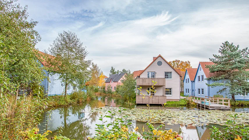 Lägenhetshus vid en av sjöarna på området. Det är tidig höst med gula löv och ljusblå himmel.