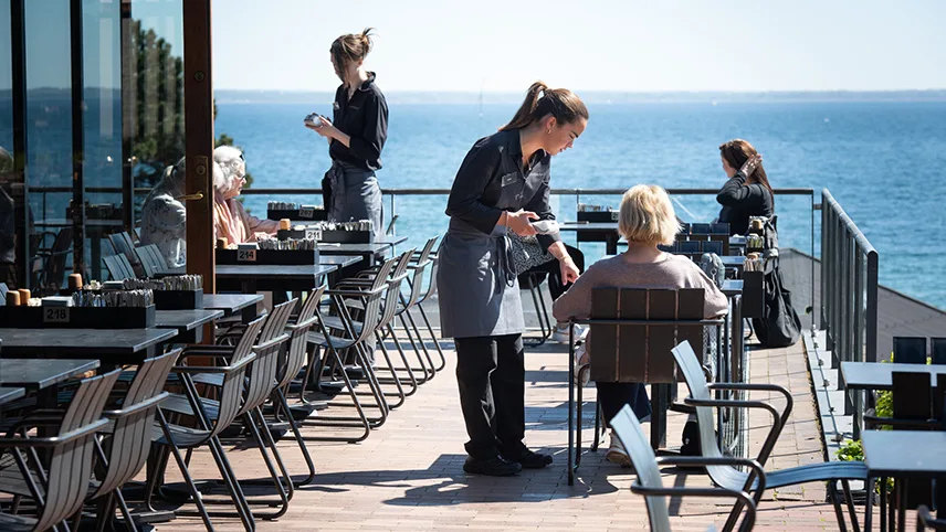 Besökare sitter på verandan vid Louisianas café och njuter av en fika i solen.
