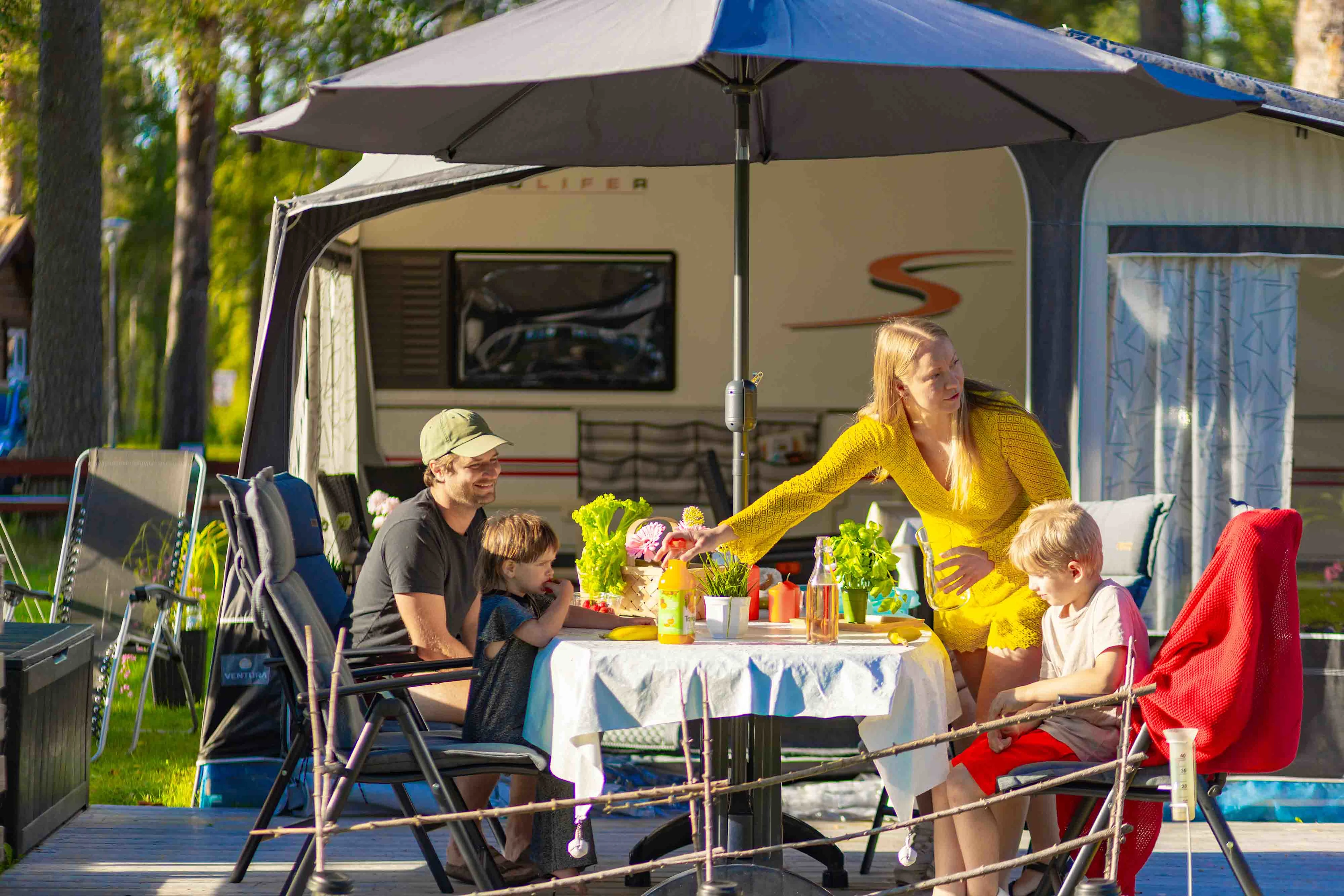 Famile foran campingvogn spiser frokost ved bord.