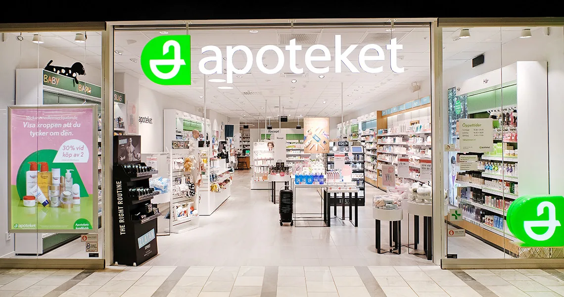 Et apotek med store glasdøre udstiller sine varer på hylder og borde i et godt oplyst og organiseret miljø.