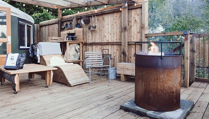 Verandan vid en av jurterna, med loungemöbler i trä, ljusslingor och ett eldfat för grillning,