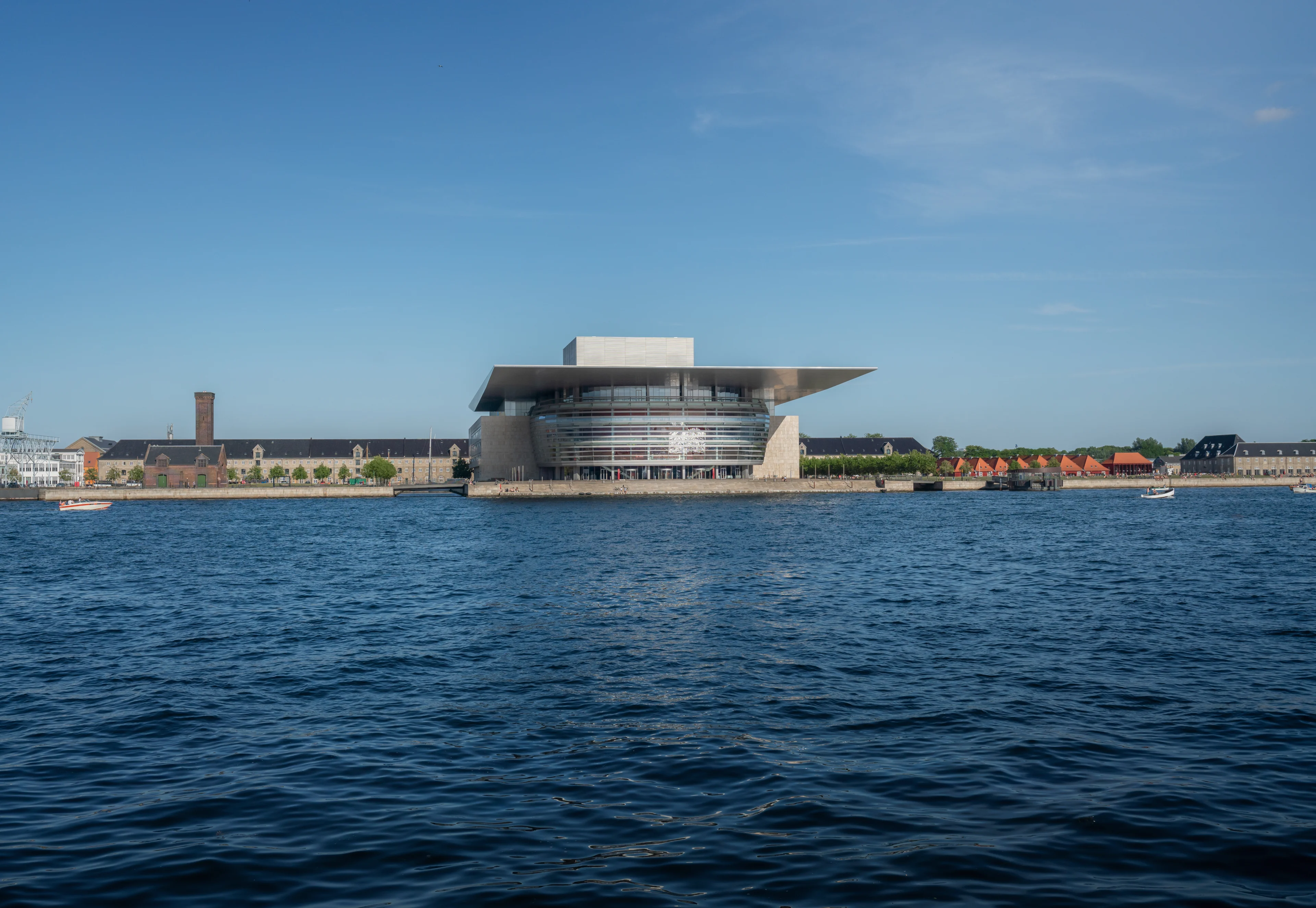 Köpenhamns Operahus mot blå himmel och med vattnet som förgrund.