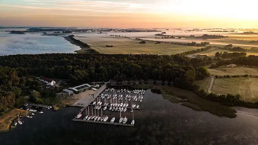 im-Jaich Naturoase Gustow sett från luften. Man ser byggnder och en småbåtshamn i ett vackert landskap med laguner och lummiga träd.