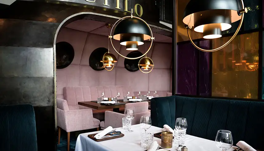 Bild från hotellets restaurang Nautilo. Matsalen är inredd med stora lampor, vackert dukade bord och mörka väggar med accentfärger i guld och ljusrosa.