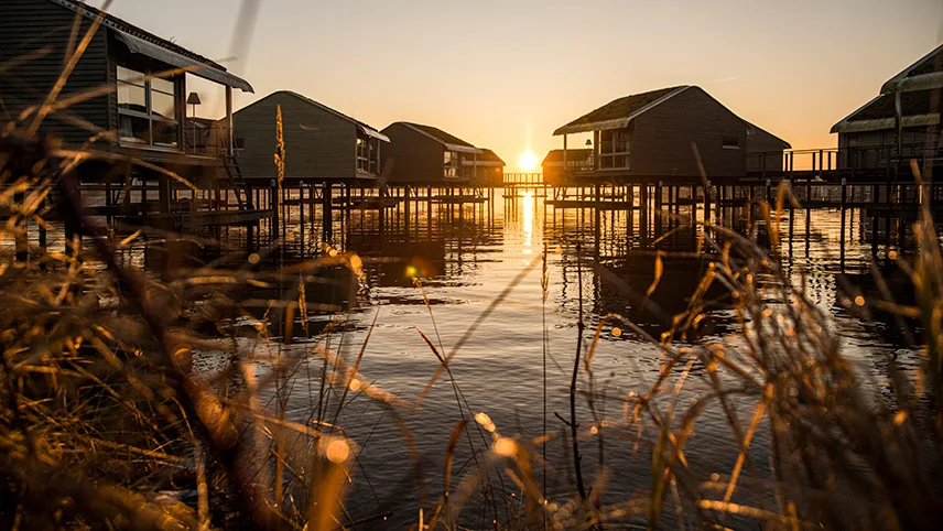 Solnedgång vid hotellet. Solen reflekteras i det blanka vattnet och i bakgrunden syns semesterhus med veranda.