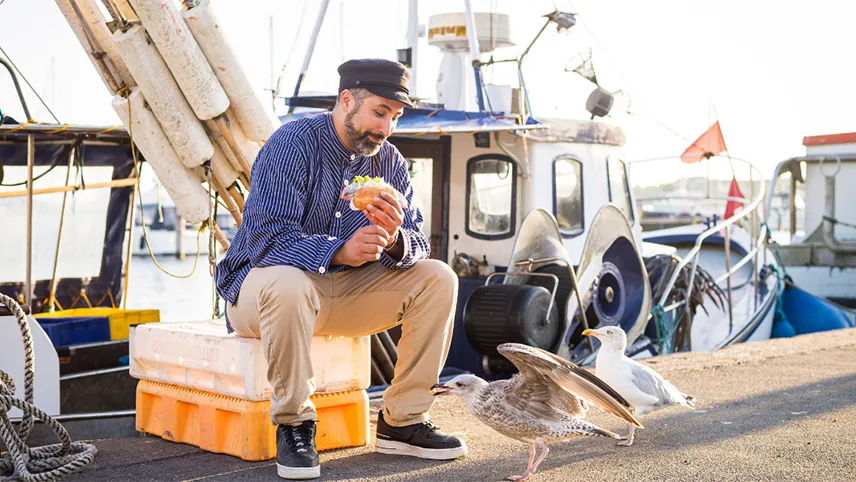 En fiskare i Lübecks hamn äter lunch och matar fåglar.