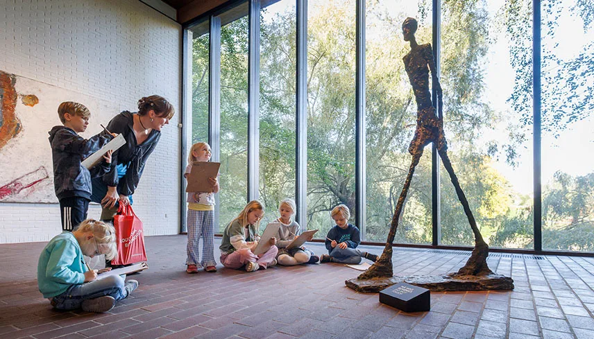 En grupp barn sitter på golvet i Giacometti-rummet och tecknar tillsammans med en lärare.