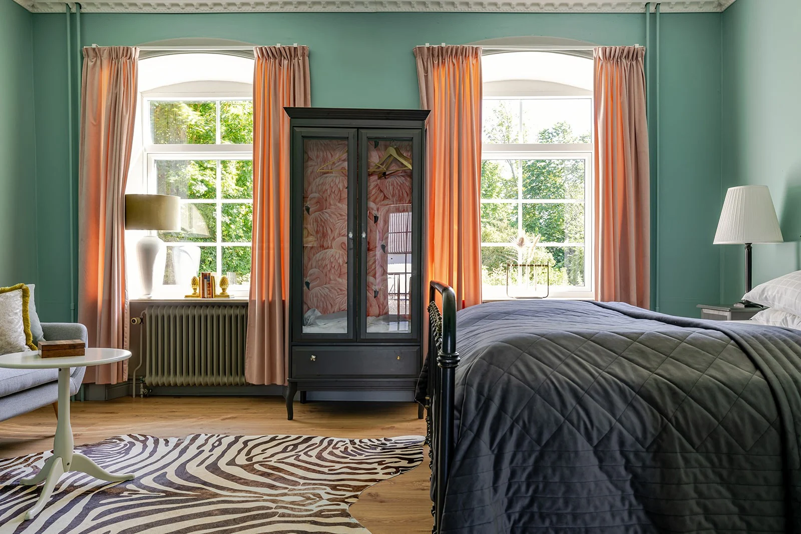 Idala Gårds hotelværelse med seng, zebragulvtæppe og grønne vægge. Solen skinner ind ad vinduerne.