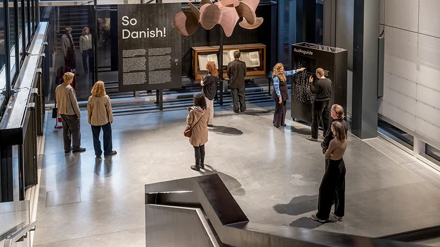 Bild från den permanenta utställningen So Danish! Besökare står framför en monter och en stor informationstavla och tittar.
