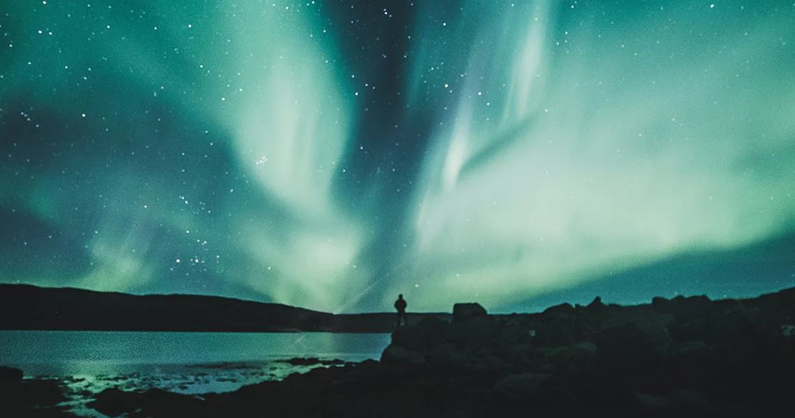 Mand står på klipper og ser på nordlys i Sverige.