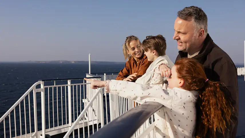 Två vuxna och två barn står på däck på fartyget och pratar och tittar ut över vattnet.