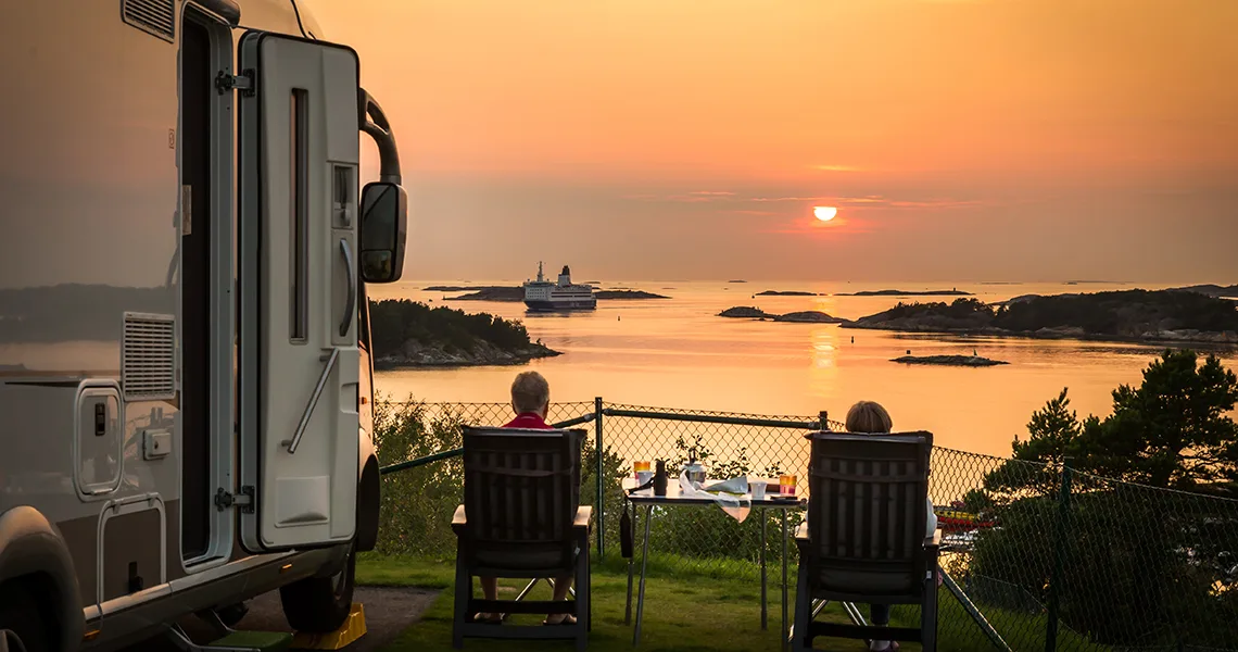 To personer i campingstole kigger ud over havet med en autocamper ved siden af dem.