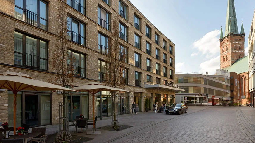Hotellets fasad med ljust tegel, stora fönster och parasoll utanför. I bakgrunden syns den berömda domkyrkan.
