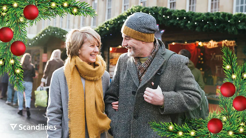 Två personer går runt på en julmarknad. De är klädda i varma kläder och ler mot varandra.