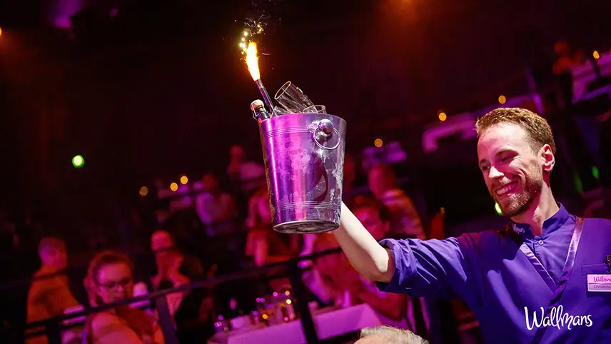 En servitör går runt bland publiken med en ishink med champagne och tomtebloss.