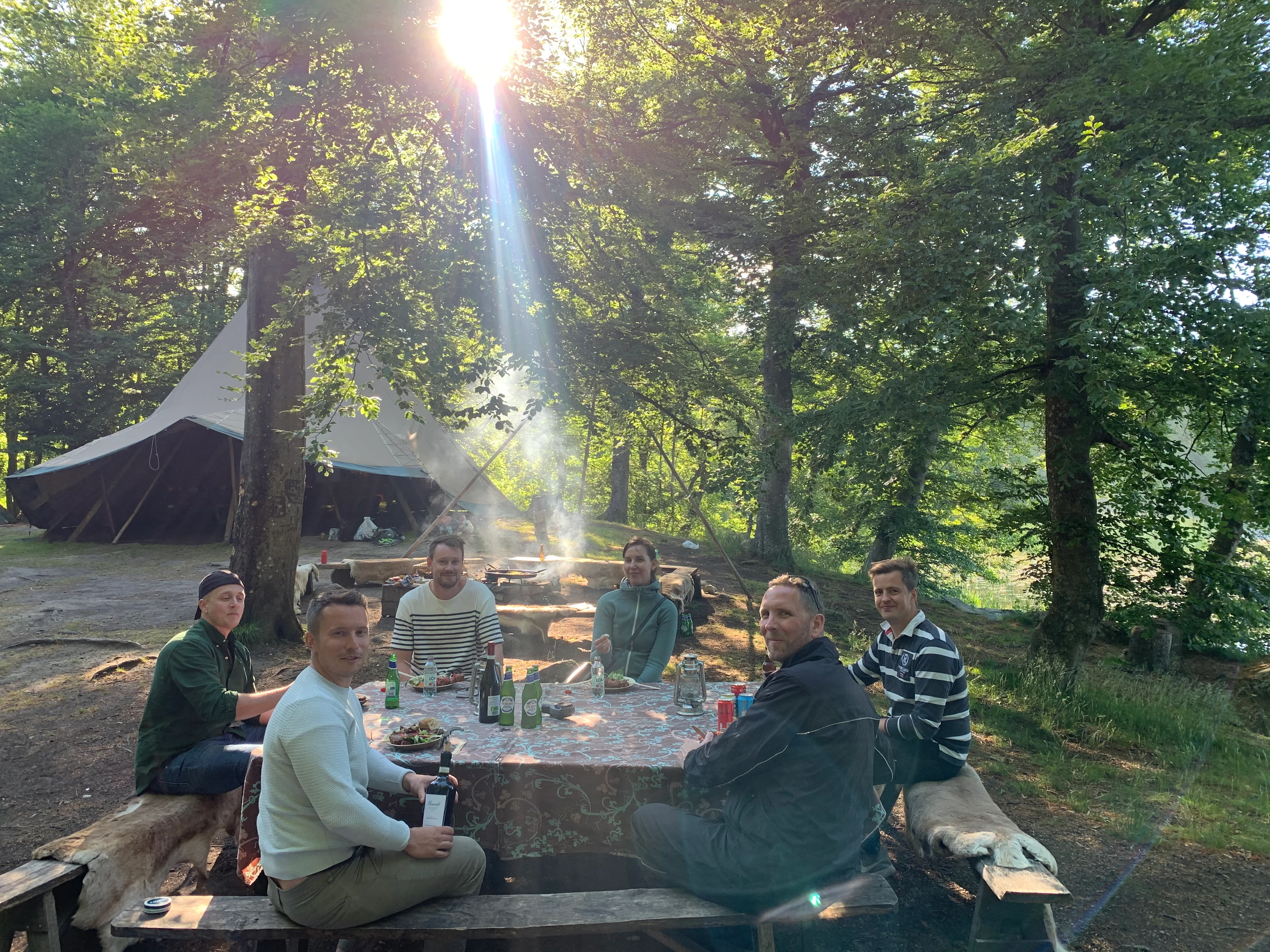 Gæster omkring et frokostbord i skoven med glampingtelte i baggrunden hos Camp hackeberga.