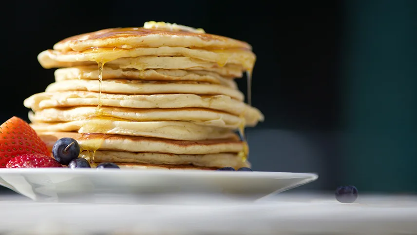 En tallrik med en hög amerikanska pannkakor med sirap och frukt.
