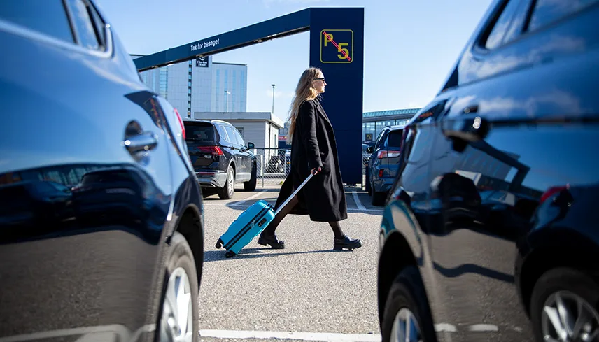 Bild från P5 vid Flygplatsen. I förgrunden syns parkerade bilar och i bakgrunden syns portalen där man kör in till parkeringsplatsen. En person kommer gående med en kabinväska på hjul efter sig.
