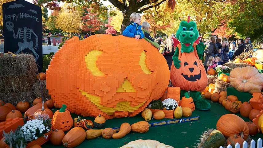 En stor pumpa i LEGO, omgivet av pynt och en maskot iklädd en pumpa-dräkt.