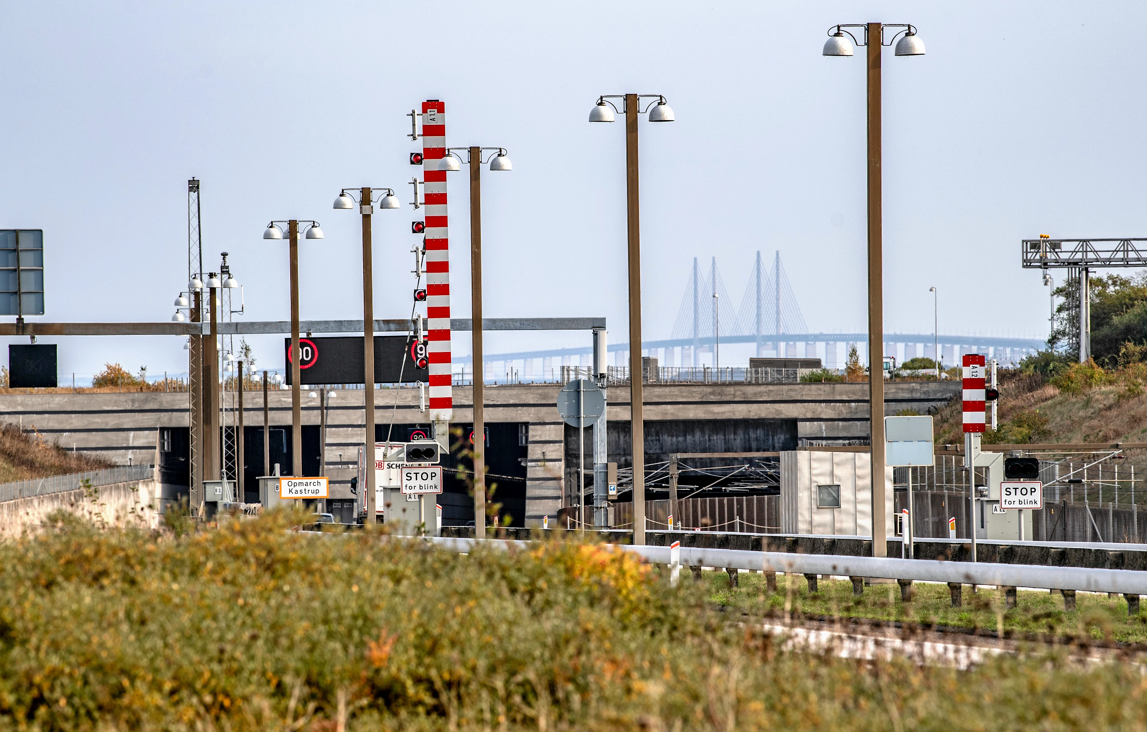 Bild av järnvägsrälls på väg in mot tunneln och med Öresundsbron i bakgrunden mot blå himmel.