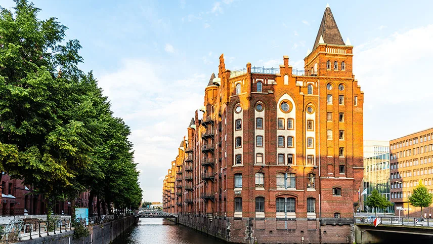 Tegelbyggnad, kanal och lummiga träd i Altstadt i Hamburg.