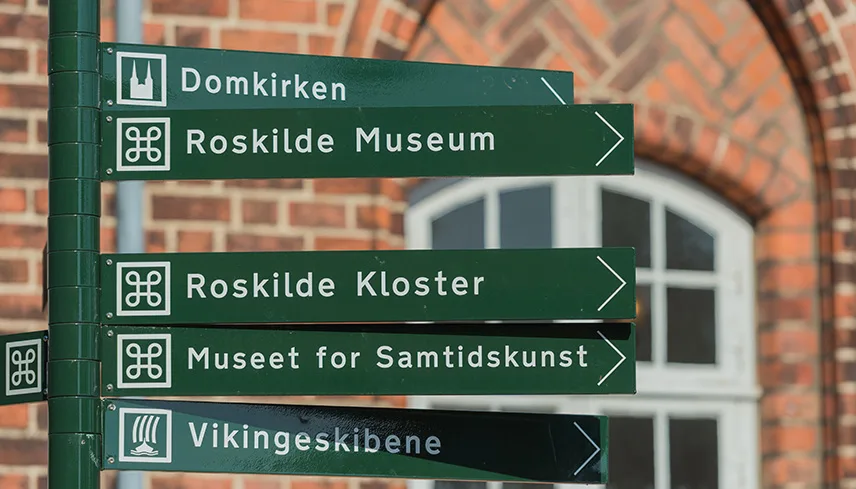 Bild av en grön stolpe med skyltar till Roskildes största sevärdheter. Skyltarna har symboler för sevärdhet, kyrka och museum och det står namnet på attraktionerna: Domkyrkan, Roskilde Kloster etc.