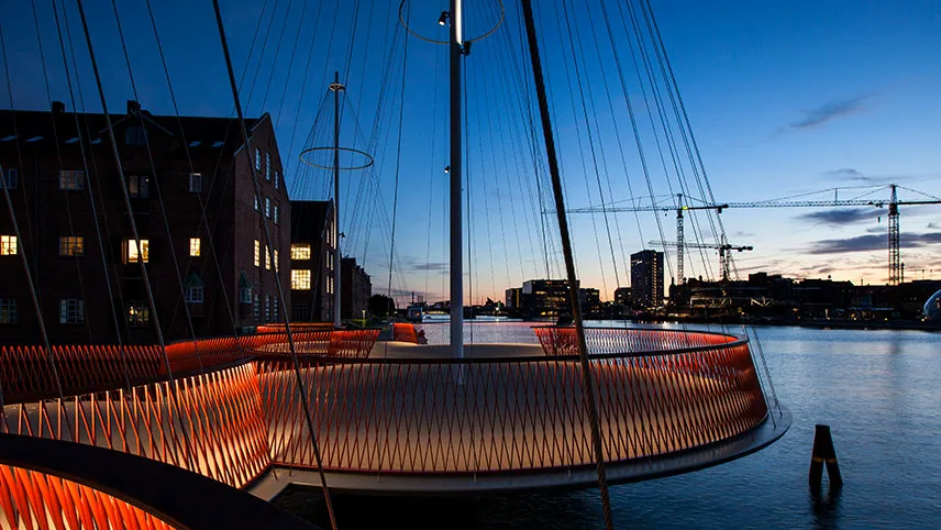 Cirkelbroen i skymningen, sedd mot en midnattsblå himmel och det spegelblanka vattnet i hamnen.