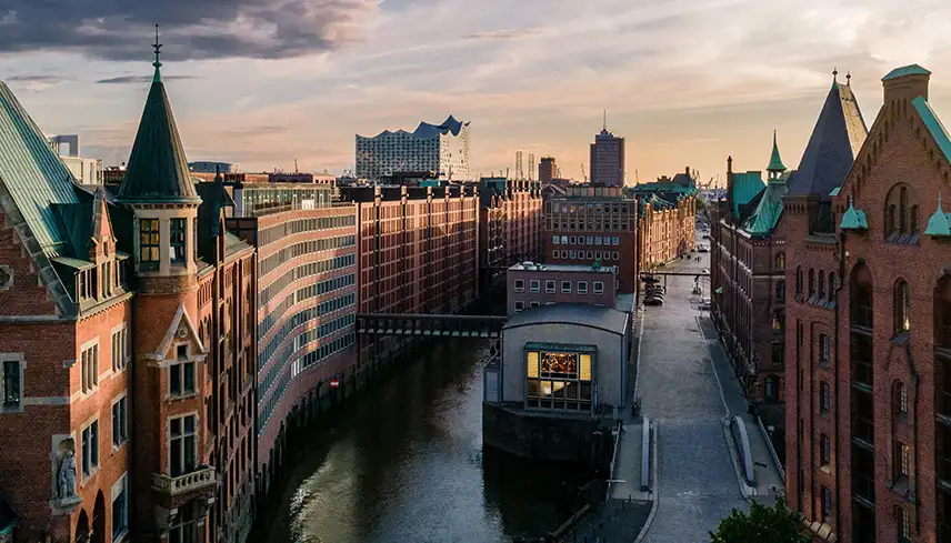 Bild av stadsdelen Speicherstad med klassiska röda tegelbyggnader, kanaler och gångbroar emellan. Det är skymning och himlen är rosa och ljusblå.