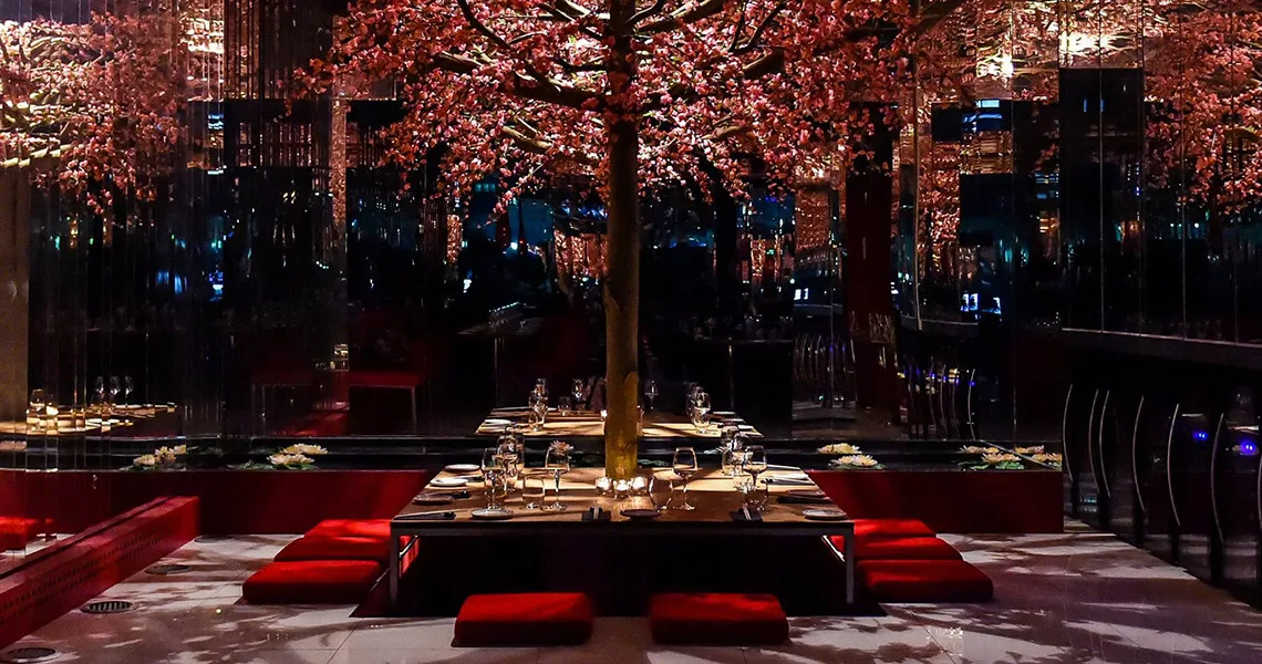 Restaurantmiljø med lave stole og borde og træer mellem bordene.