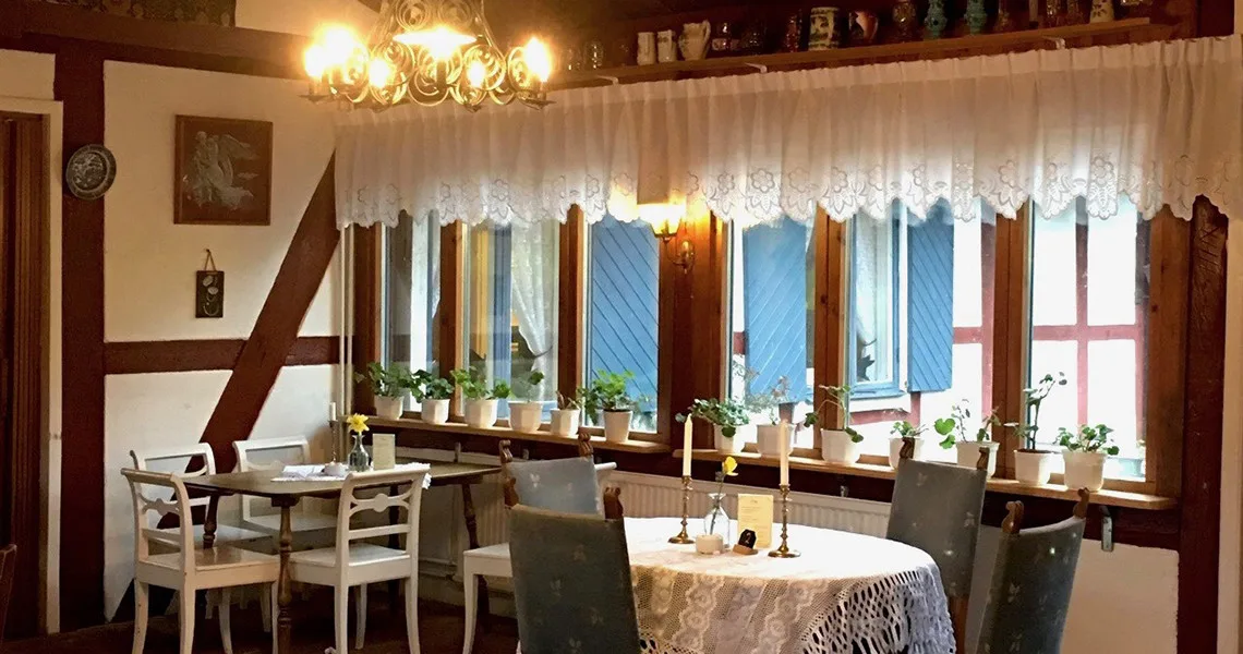 Sittplatser  med antikke sofaer og sirlige gardiner i vinduerne på Kaffestugan Annorlunda.