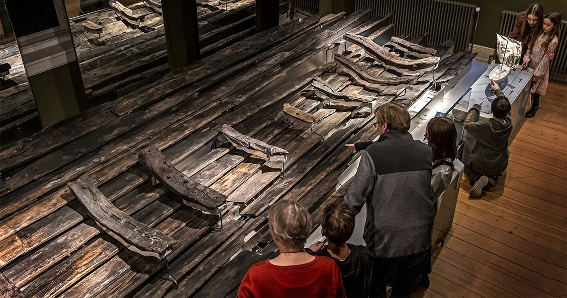 Museibesökare tittar på gamla träplankor som varit en båt.