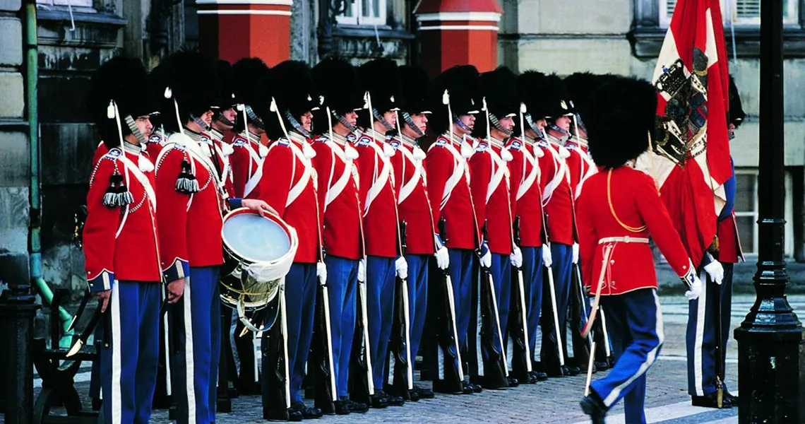 Slottsvakter som står på rad med röda och blå uniformer och svarta hattar.