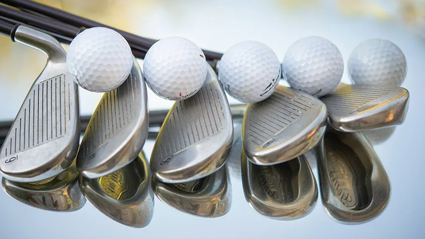 Fem golfklubbor ligger på en yta med fem golfbollar balanserades ovanpå.