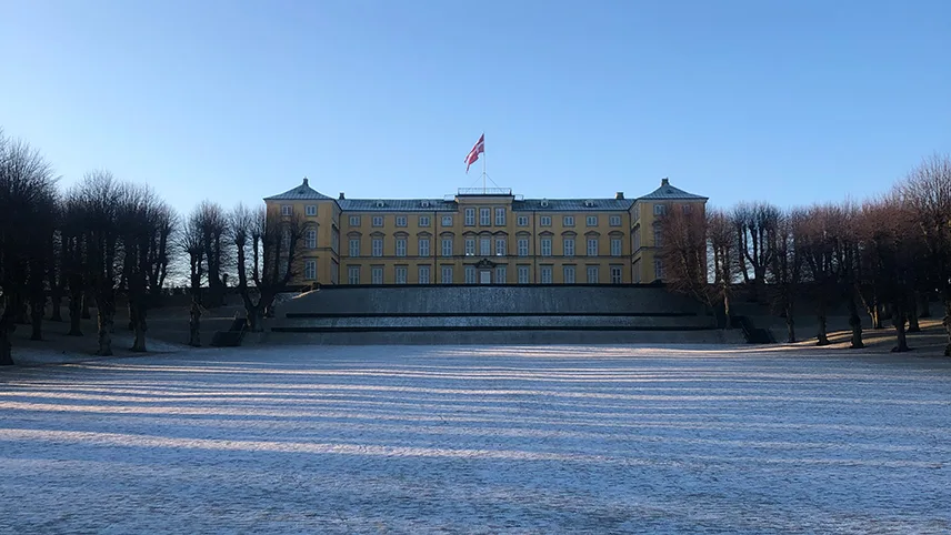 Frederiksbergs slott i vintertid med snöklädd mark, blå himmel och slottet som dominerar landskapet i bakgrunden.