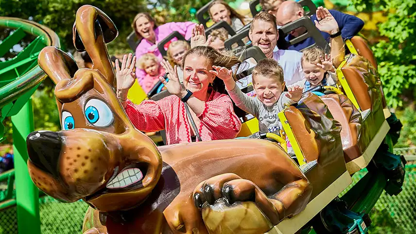 En liten bergochdalbana med glada besökare som har händerna i luften.