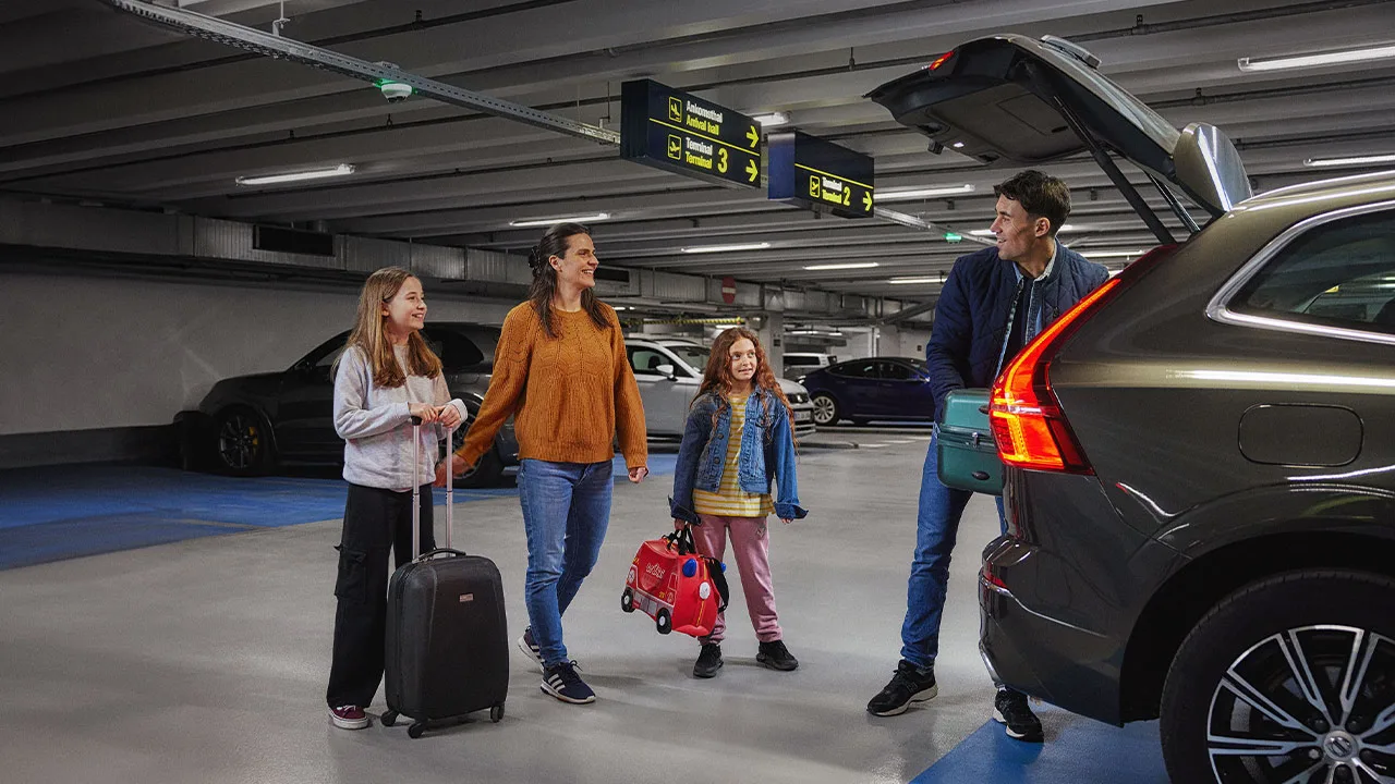 En familj med två föräldrar och två barn parkerar i ett parkeringshus och gör sig redo att gå in på flygplatsen.