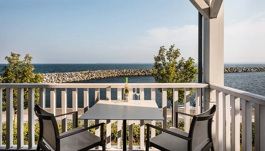 Utsikten från en veranda. Två stolar och ett bord står vända ut mot vattnet och man ser havet och en stenpir.